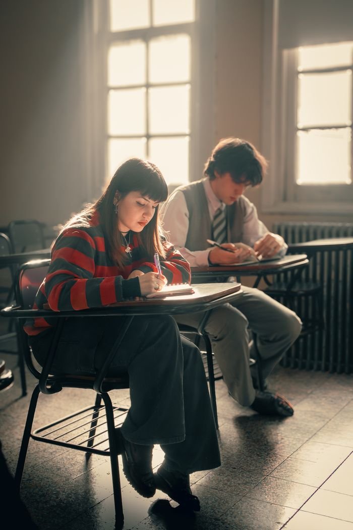 Two students focus on writing assignments under soft classroom lighting.